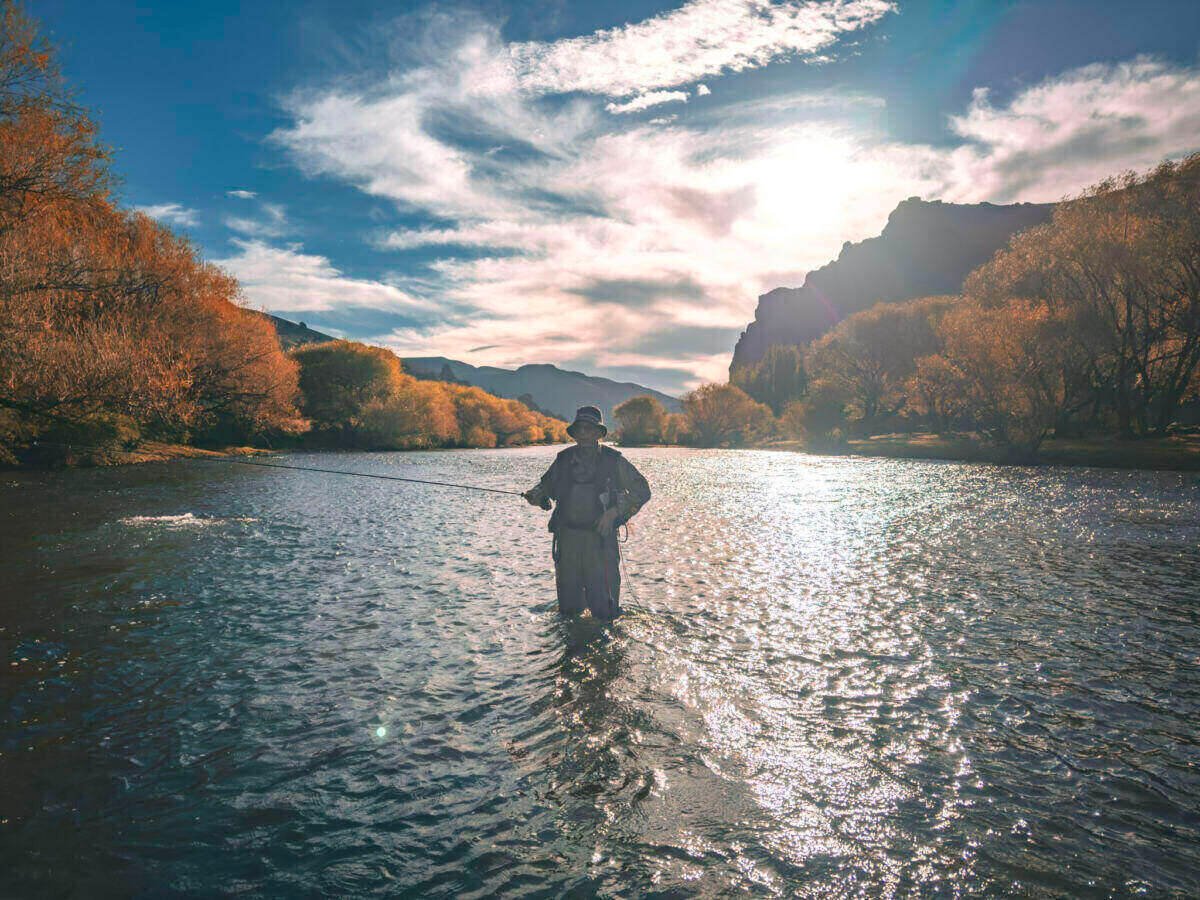 Angler wading a river at sunset among autumn colors in late season, Argentine Patagonia
