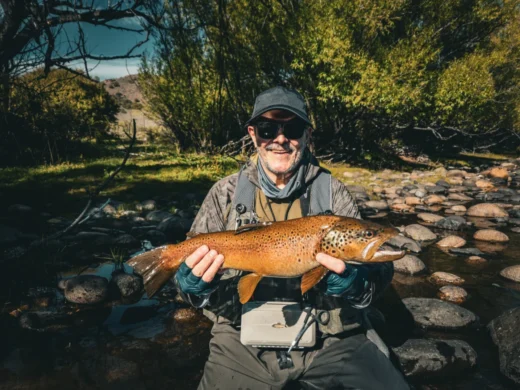 Angler kneeling on the bank with a heavy brown trout