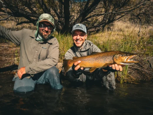 Two anglers in the river holding up a brown trout together