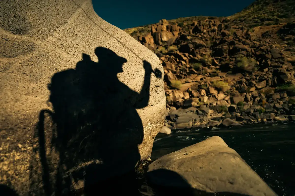 Shadow of a fly fisherman with rod raised on an Argentine riverbank