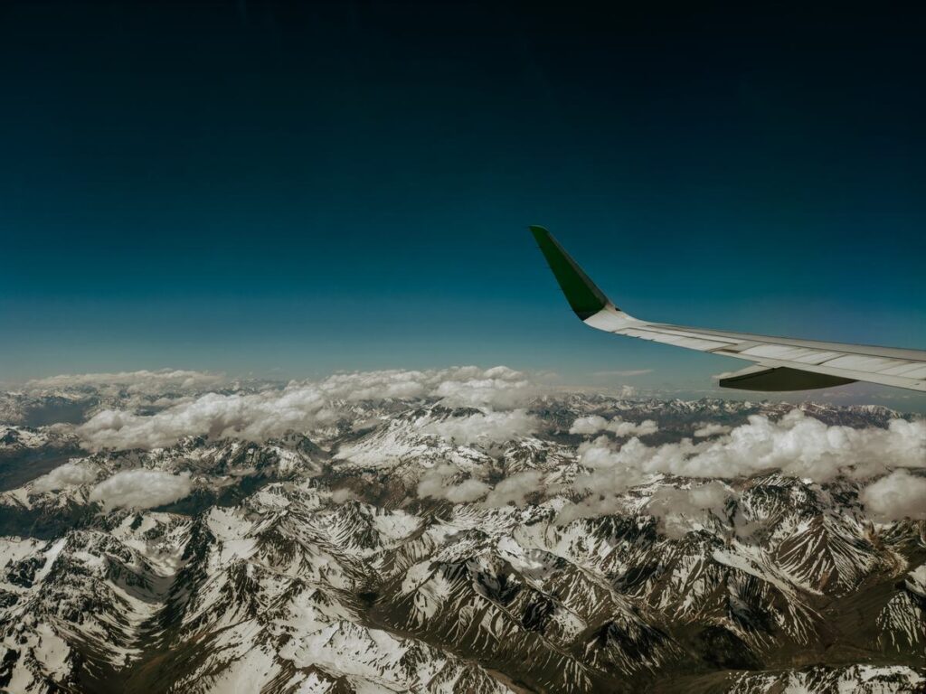 Snow-covered peaks of the Andes under scattered clouds, seen from the window of a domestic flight with the wing in the foreground
