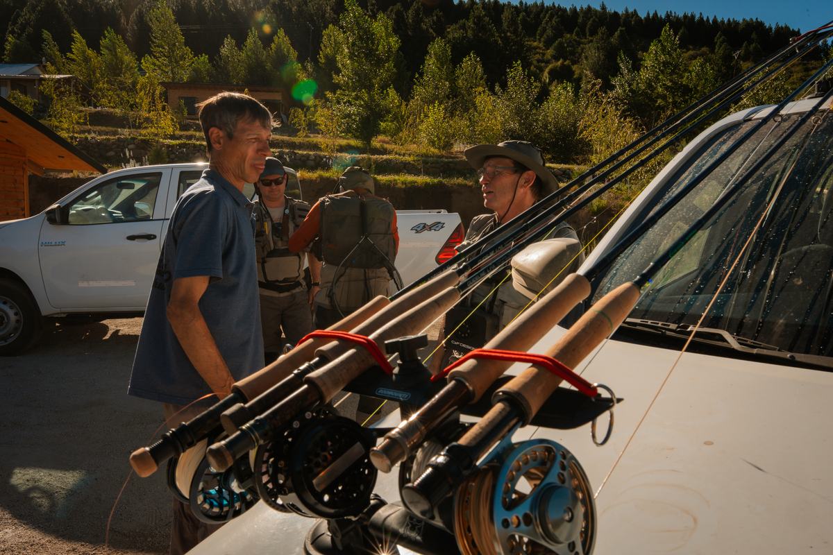 Fly rods and reels racked on the hood of a pickup truck while guests and guides talk in the morning sun, Patagonia