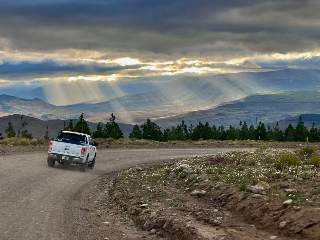 Dirt ranch road through northern Neuquén with a pickup truck heading toward the hills under rays of evening light